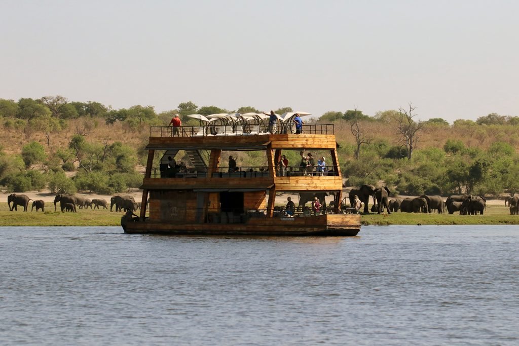 A large wooden cruise ship on the Chobe River with tourists watching Elephants in the Safari