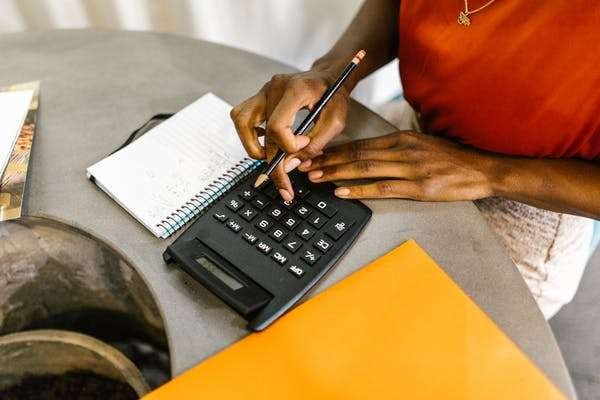 A lady wearing red, pressing an office calculator as she calculates budget related finances