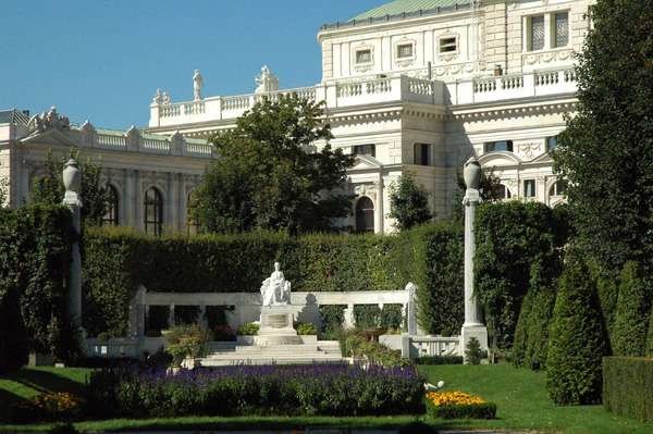 Volksgarten (People's Gardens, Austria). A large white-painted building with multiple coloured flowers and trees surrounding it.