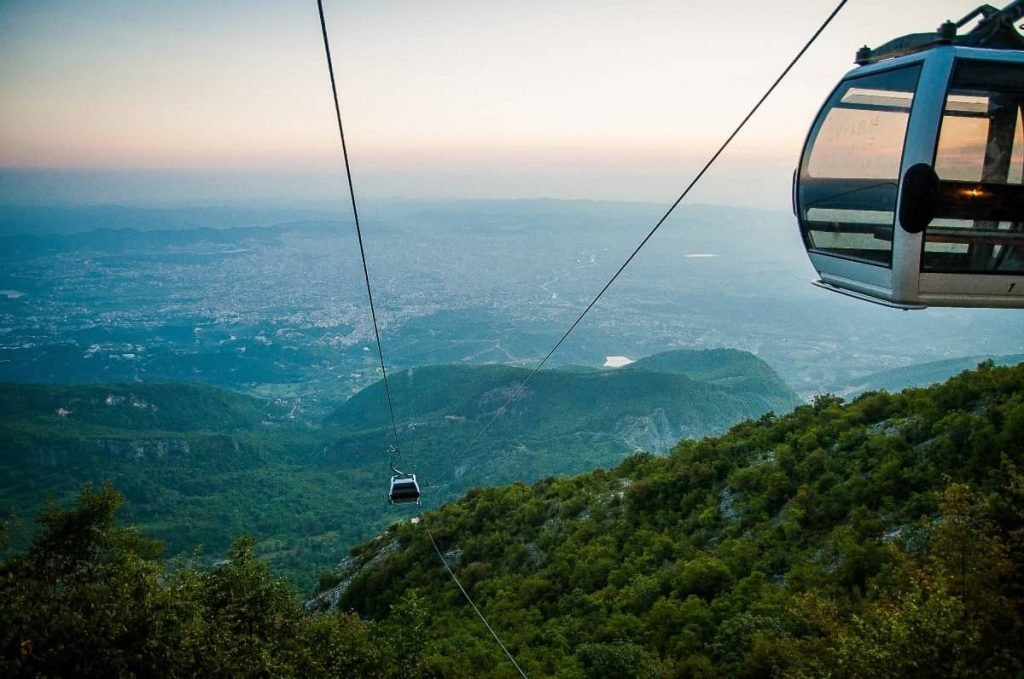 a cable car flying over green forests in one of the memorable places to visit in Tirana, Albania.