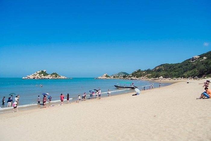 people on a sandy beach in front of a blue ocean and one of the fun places to visit in Shantou, China.