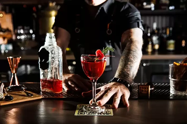 Bar tender holding a glass of a red cocktail