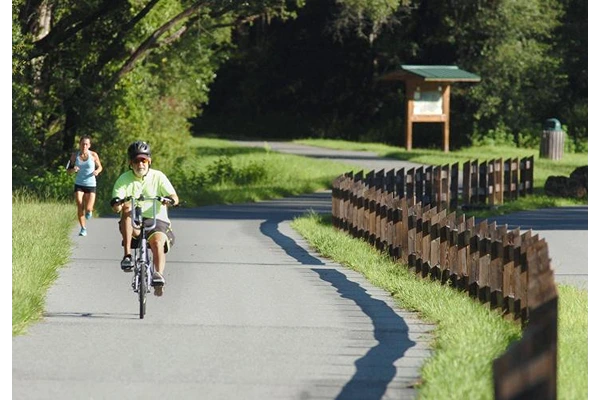 A man riding a bicycle along a smooth trail with a woman jogging behind him.