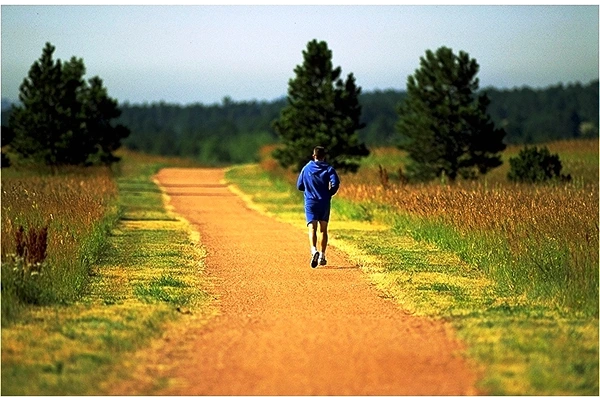 A man jogging on a trail with trees around and in the distance
