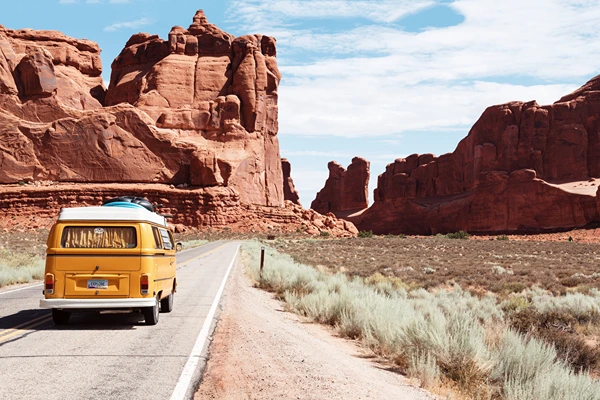 A yellow bus driving on the road surrounded by mountains