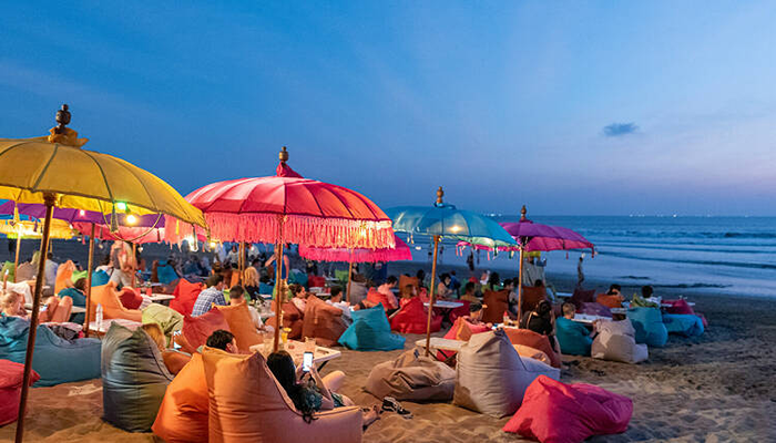 A beach in the evening with lots of lit colourful umbrellas