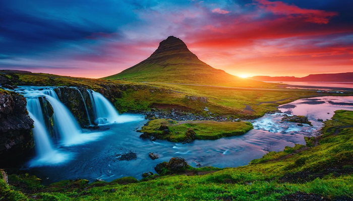 A lovely evening scene. Three beautiful waterfalls overflowing into a stream surrounded by a vast green-land and a mountain in the background.