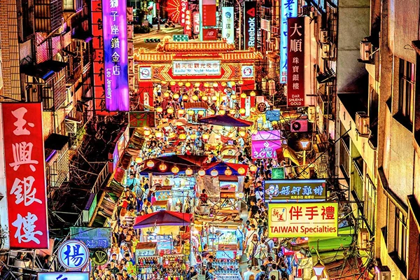 A busy street in Taiwan with colorful lights, many neon signs and people walking around.