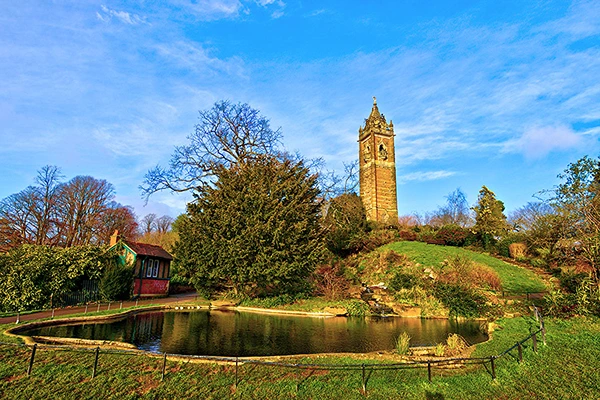 The Cabot tower in Bristol surrounded by a pond, some trees and beautiful greenery. 