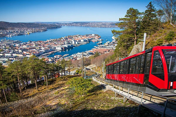 Mount Fløyen showing the waters with lots of boats and houses for tourists and also a red mini train riding tot he top of Mount Fløyen.
