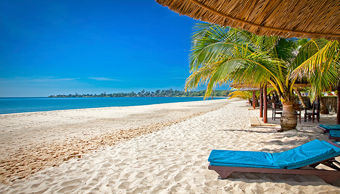 A beach with blue waters that correspond to the clear blue skies, blue seats under huts and palm trees