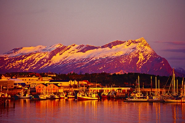 Mount Rønvikfjellet in Bodø with red skies, gold looking mountains, and bright lights in the evening.
