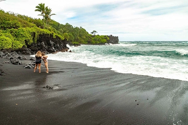 A beach with two ladies standing on the black sand shore