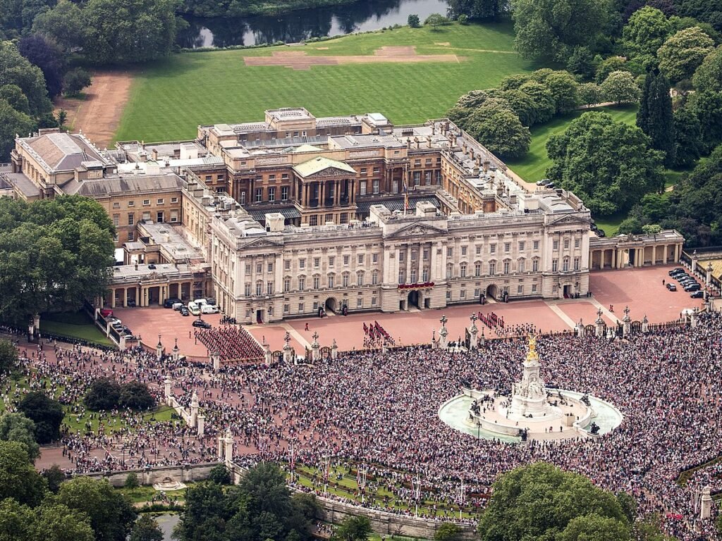 Aerial view of Buckingham Palace showing the architectural masterpiece and the front surrounded by a vast number of people