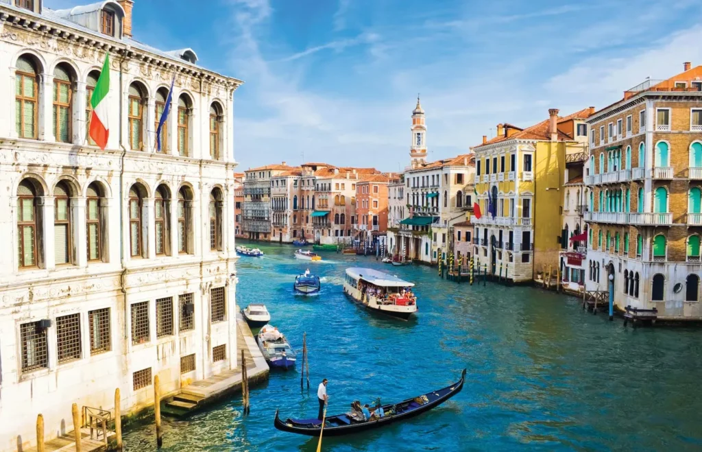 A city in Venice Italy, with colourful houses alongside a river with boats carrying visitors